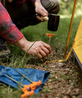 Person using hammer to install Beefy 10-Inch Steel Tent Stakes Heavy-Duty Ground Anchors 4-Pack for camping in grass