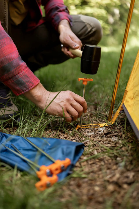 Person using hammer to install Beefy 10-Inch Steel Tent Stakes Heavy-Duty Ground Anchors 4-Pack for camping in grass