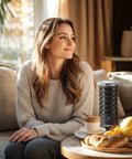 Woman sitting on couch next to 4 In 1 Electric Milk Frother For Hot And Cold Foam, Temperature Control And Auto Shut Off.