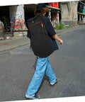 Person walking on street with black Oxford Fabric dumb drum storage bag on back, showcasing practicality for gig loads and campouts.