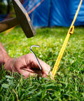 Heavy Duty Aluminum Tent Stakes 20 Pack 7 Inch Ground Stakes With Hooks being hammered into grass for camping tents