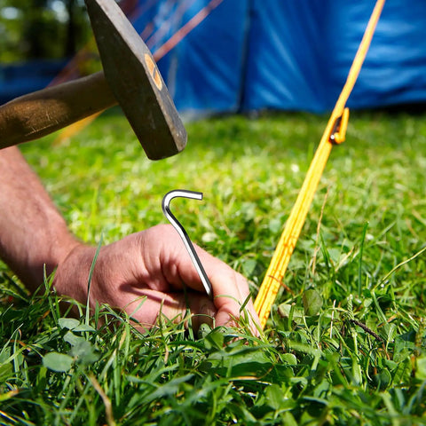 Heavy Duty Aluminum Tent Stakes 20 Pack 7 Inch Ground Stakes With Hooks being hammered into grass for camping tents