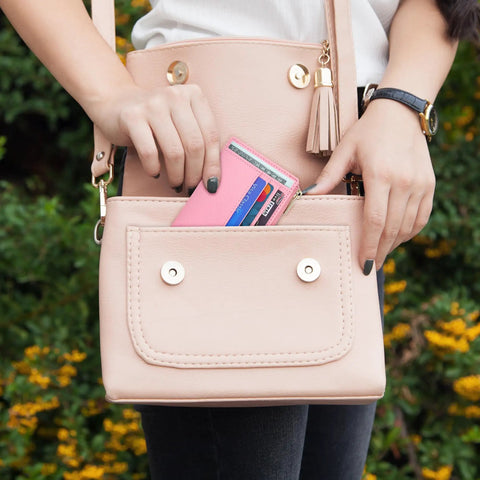 Woman placing slim RFID blocking wallet for women with front pocket card case, 6 card slots, ID window, chic pink, into purse