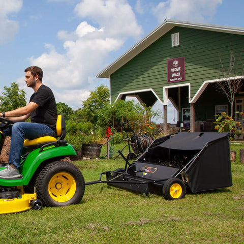 Man using 40 Inch Tow Behind Lawn Sweeper With Dethatcher And Hamper Windscreen attached to tractor for yard cleanup