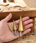 Hand holding three titanium plated step bits from Six Piece High Speed Reaming Pagoda Sawtooth Drill Bit Set With Titanium Plating In Box