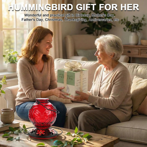 Two women exchanging a hummingbird feeder gift indoors, with a red Outdoor Hummingbird Feeder 25 Oz With Perch And Five Flower Ports in foreground.