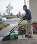 Deluxe Triple Brush Push Power Sweeper Boasts 38 Inch Wide Cleaning Deck And Huge 13 2 Gallon Hopper in use outdoors.