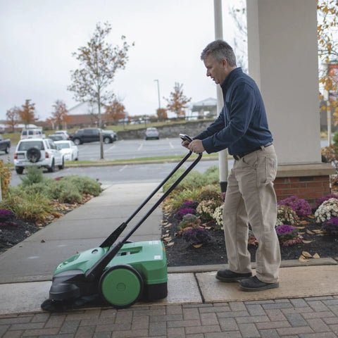 Deluxe Triple Brush Push Power Sweeper Boasts 38 Inch Wide Cleaning Deck And Huge 13 2 Gallon Hopper in use outdoors.