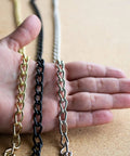 Hand holding 12 gauge solid steel twist link fixture chains in different finishes, part of the 164 ft reel for pendant lighting and decor.