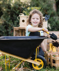Child playing with six piece kid friendly wheelbarrow and garden tool set with apron and gloves for backyard play