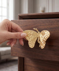 Heavy Duty Butterfly Cabinet Knobs With Slick Brushed Gold Finish For Dressers, solid brass handle grasped on wooden drawer.