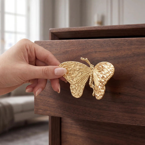 Heavy Duty Butterfly Cabinet Knobs With Slick Brushed Gold Finish For Dressers, solid brass handle grasped on wooden drawer.