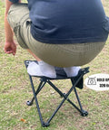 Person sitting on 2 Pack 13 Inch Portable Folding Camping Stool with Carry Bag, demonstrating weight capacity of 320 lbs on grass.