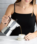 Woman pouring coffee from Stovetop Moka Pot Espresso Maker For Home Brew 6 Cup Greca Style Coffee Pot in Silver into cup