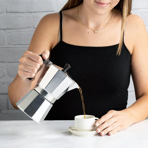 Woman pouring coffee from Stovetop Moka Pot Espresso Maker For Home Brew 6 Cup Greca Style Coffee Pot in Silver into cup