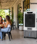Heavy Duty Portable Evaporative Air Cooler With 12000 CFM Hella Badass Cooling For Large Indoor Outdoor Spaces Sweet Chill With 12 Hour Timer Smart App Remote Control next to two women in a cafe.