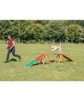 Dog on agility walk ramp with color-coded zones in park, trainer beside. Agility Dog Walk Ramp With Color Coded Contact Zones For Safe Training.
