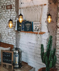 Three Pack Battery Operated Outdoor Chandelier Pendant Lights With Rustic Black Metal Bell Shade For Gazebo Patio Porch Decor hanging over books and a cactus.