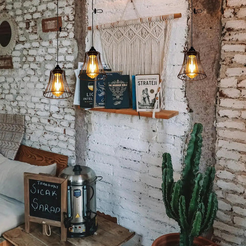 Three Pack Battery Operated Outdoor Chandelier Pendant Lights With Rustic Black Metal Bell Shade For Gazebo Patio Porch Decor hanging over books and a cactus.