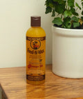 Bottle of Beeswax Wood Polish And Conditioner With Orange Oil for Furniture Feed-N-Wax on a wood surface next to a plant.