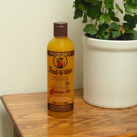 Bottle of Beeswax Wood Polish And Conditioner With Orange Oil for Furniture Feed-N-Wax on a wood surface next to a plant.