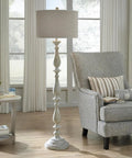 Bernadate Cottage Candlestick Floor Lamp, 61 Inch Tall, whitewashed cast resin base with drum shade next to a gray armchair