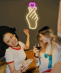 Finger Heart Neon Sign In Pink And Warm White For Bedroom And Game Room LED Light Hand Gesture Decor above two people on couch