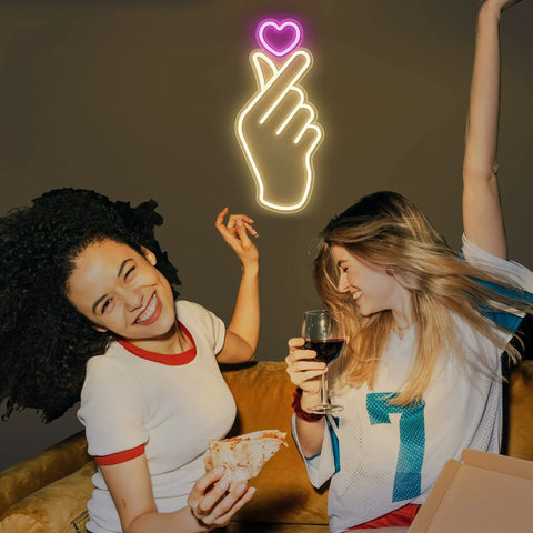 Finger Heart Neon Sign In Pink And Warm White For Bedroom And Game Room LED Light Hand Gesture Decor above two people on couch