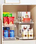 Super Handy Two Tier Under Sink Organizers And Bathroom Storage Solutions For Cabinets And Kitchen Pantries With Smooth Slide Out Drawers And Fully Adjustable Dividers In Bright White Two Pack holding snacks, drinks, and packages.