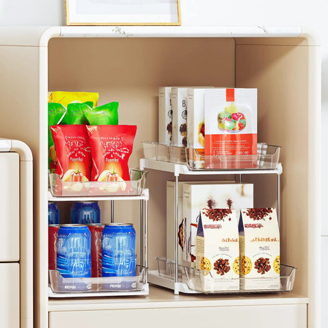 Super Handy Two Tier Under Sink Organizers And Bathroom Storage Solutions For Cabinets And Kitchen Pantries With Smooth Slide Out Drawers And Fully Adjustable Dividers In Bright White Two Pack holding snacks, drinks, and packages.