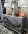 Modern dresser with marble pattern, gold handles, and two lamps, topped with decor and mirror, complements luxury bedroom decor.