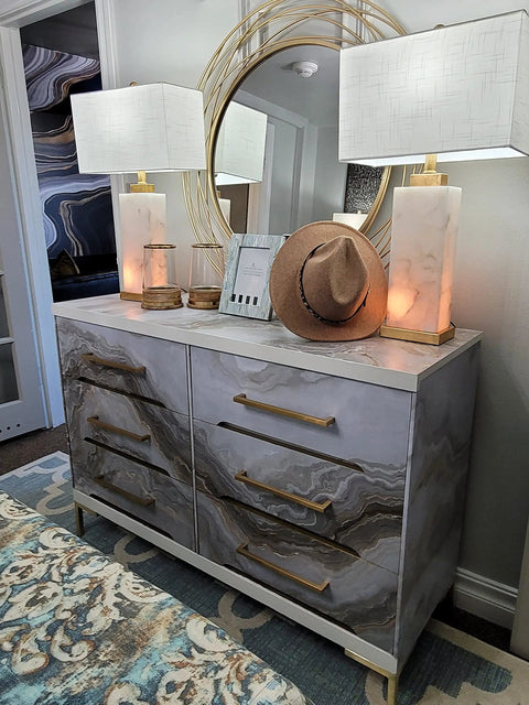 Modern dresser with marble pattern, gold handles, and two lamps, topped with decor and mirror, complements luxury bedroom decor.