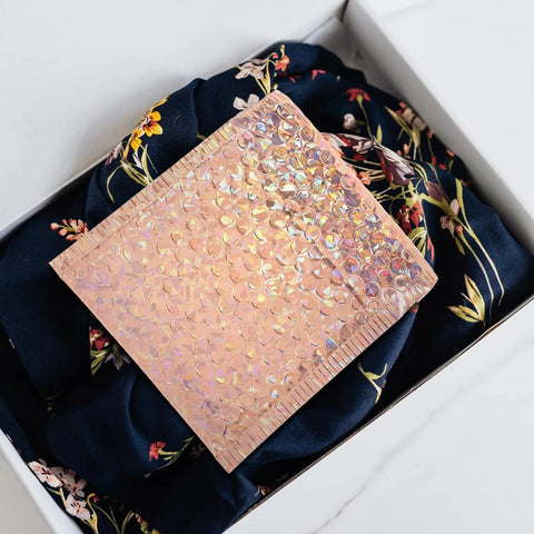 Close-up of rose gold padded mailer on floral fabric, part of Rose Metallic Padded Mailers 20 Pack 6x5 Inch Self Sealing Cushioned Shipping Bags For Mailing Clothes And Small Packages Durable Protective Packaging That Just Works For Quick Ship
