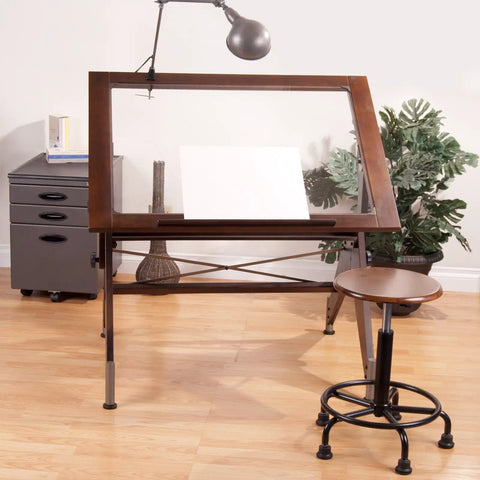 Retro Stool In Rustic Oak Finish With Pneumatic Height Adjustment From 19 To 26 Inches, next to a drafting table in an art studio.