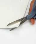 Gasket paper sheet being cut by blue Scott Titanium scissors