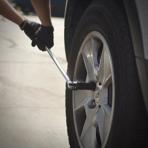 Person using a half inch drive breaker bar with flexible head twenty four inch length chromoly construction on a car tire lug nut