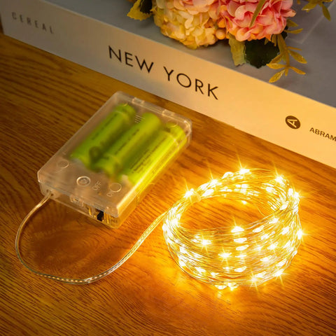 Coiled warm white Fairy String Lights 33 Ft Long Battery Operated 100 LED Copper Wire Twinkle Lights on a wooden table.