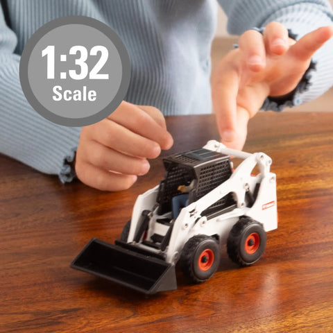 Child playing with Bobcat Skid Steer Construction Toy Set 1:32 Die Cast on table with bucket attachment visible.