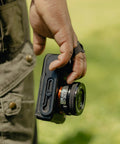 Photographer holding camera with Micro Clutch L Plate Hand Strap For Mirrorless Cameras Low Profile Finger Loop With Battery Access ARCA
