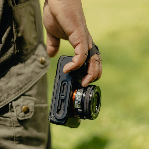 Photographer holding camera with Micro Clutch L Plate Hand Strap For Mirrorless Cameras Low Profile Finger Loop With Battery Access ARCA