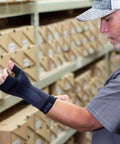 Man adjusting WS6 Compression Wrist Sleeve for Carpal Tunnel Relief and All-Day Pain Support in warehouse.