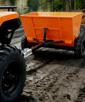 71 Gallon Tow Behind Sand And Salt Spreader For Snow And Ice Control, bright orange ATV attachment on dirt trail.