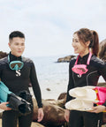 Two divers on rocky beach with wetsuits, snorkeling gear, and dive fins.