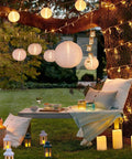 Outdoor scene with 12 Pack White LED Paper Lanterns in various sizes hanging from a tree, creating a cozy evening atmosphere.