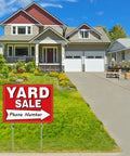 Yard sale sign on lawn, red sign with white 'YARD SALE' text and arrow, mounted on two metal stakes.