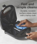 Hamilton Beach Electric Sealed Sandwich Maker Grill For Hot Pockets And Grilled Cheese, nonstick surface being wiped clean.