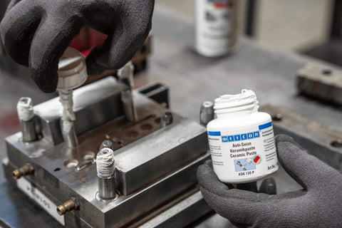 Anti Seize Ceramic Paste For Screws And Bolts High Temp Metal Free Lubricant being applied to threaded fasteners on metal block