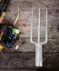Three-Prong Fish Fork Beefed-Up Heavy Duty Steel Garden Tool For Fishing And Harvesting Ergonomic Handle next to fishing rods