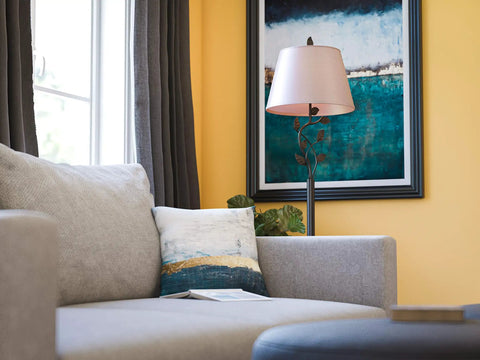 Ashlen Oil Rubbed Bronze Table Lamp With Gold Tapered Shade Rustic Living Room Lighting beside gray couch, art in background.
