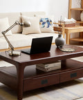 Modern living room with wooden coffee table, laptop, and decorative items; sofa and shelf in background.